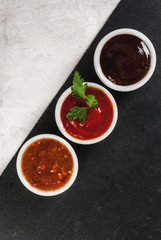 Three kinds of red tomato sauce on a white stone table: traditional classic ketchup, barbecue sauce, sweet and sour Chinese sauce. Top view copy space