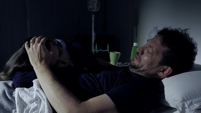 Sad sick man in hospital bed crying caressing sleepy girlfriend