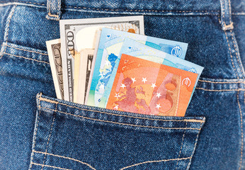 Different banknotes of Euro and american currency sticking out of the back jeans pocket. Money in jeans pocket for travel and shopping
