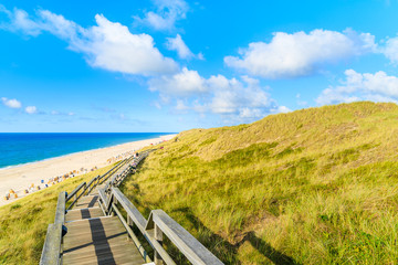 Fototapeta na wymiar Wooden walkway along a coast of North Sea and view of beautiful beach near Wenningstedt village, Sylt island, Germany