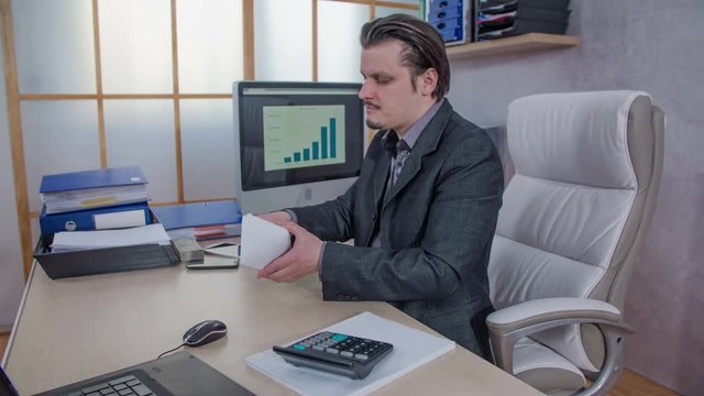 A businessman is grabbing an envelope and he is taking some money out of it and putting it back into his pocket. Then he is putting the envelope back on the table.
