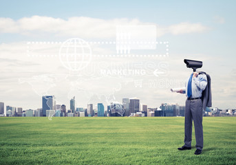 Camera headed man standing on green grass against modern citysca