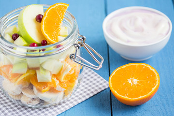 Various fruits in a glass jar with yogurt and orange on a wooden table