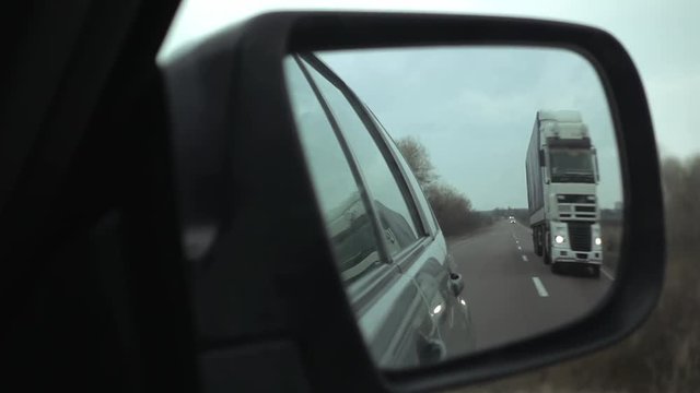 Car overtakes the truck on interurban highway. POV view to the side mirror of the car. Overtaking maneuver slow motion.