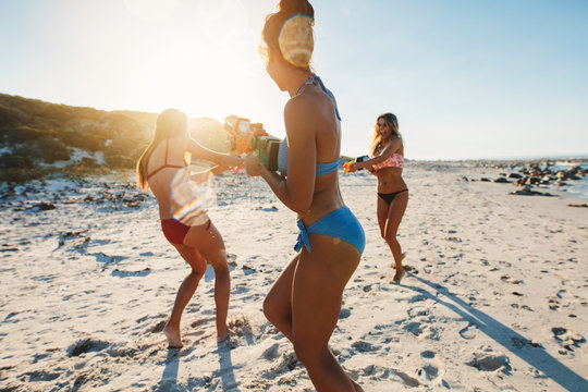 Three young women in bikini having water gun fight on beach
