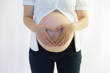 Pregnant Woman maternity concept holding her hands in a heart shape on her baby bump. Pregnant Bare Belly with fingers heart symbol.