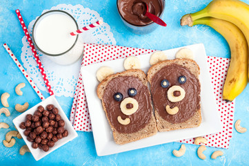 Children's breakfast with sandwiches and milk. Funny bear face sandwiches with chocolate paste, banana, nuts, and berries. Top view