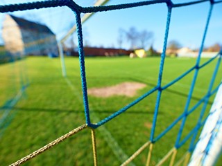 Detail of yellow blue crossed soccer nets, soccer football in goal net with grass on outdoor...