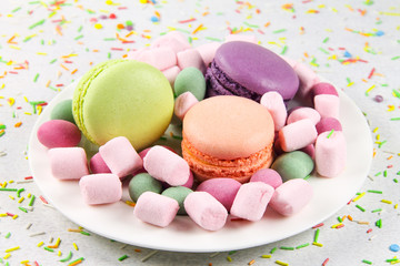 Multicolored macaroons and marshmallows on a white plate