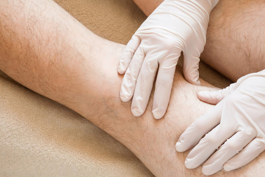 Therapist hands in protective gloves massaging man's legs.