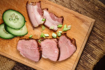 A close-up of sliced beef steak with a cucumber on a cutting board on a wooden background