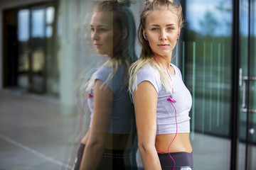 Woman In Sportswear Listening Music Against Glass Wall