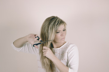 Angry blonde woman cuts her hair with scissors