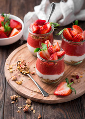 Delicious homemade granola, yogurt and strawberry parfait in glass jars on rustic wooden background