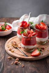 Delicious homemade granola, yogurt and strawberry parfait in glass jars on rustic wooden background
