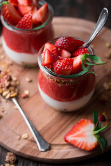 Delicious homemade granola, yogurt and strawberry parfait in glass jars on rustic wooden background