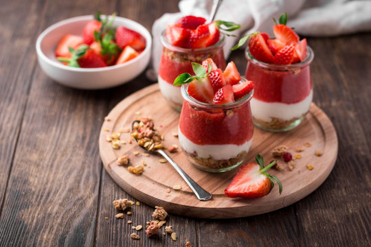 Delicious homemade granola, yogurt and strawberry parfait in glass jars on rustic wooden background