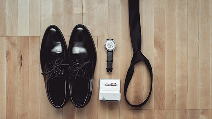 Close up of modern groom accessories. wedding rings, black necktie, leather shoes and watch