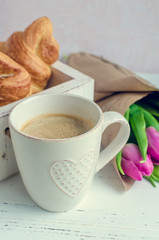 Cup of coffee with bouquet of pink tulips and croissants