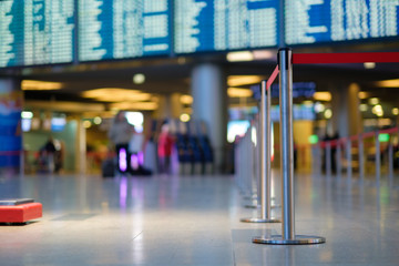 Stanchion barriers for waining lines in front of check in desks and flight schedule screens in airport on blurry background
