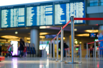 Stanchion barriers for waining lines in front of check in desks and flight schedule screens in airport on blurry background