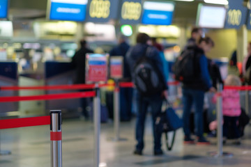 Stanchion barriers for waining lines in front of check in desks in airport on blurry background with passengers in queue