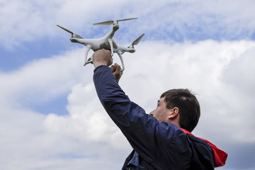 A man with a quadrocopter in his arms raised to the sky. A white drone is being prepared for the flight.
