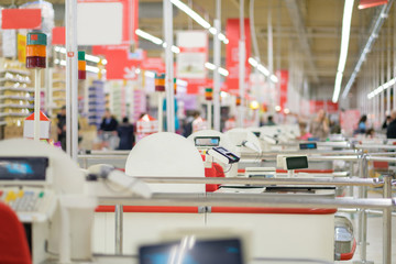 Row of cash desks with screens and card payment terminals on blurry background with shelves and customers