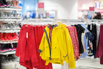 Variety of bright jeans and winter jackets and accessories on hangers in kids clothes store