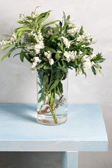 Spring snowflake Leucojum vernum bouquet in glass vase on blue wood table and gray background.