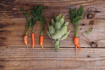 Artichoke between carrots on an old wooden table