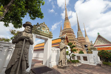 Two big Chinese statues, trees, gate and chedis at the Wat Pho (Po) temple complex in Bangkok, Thailand.