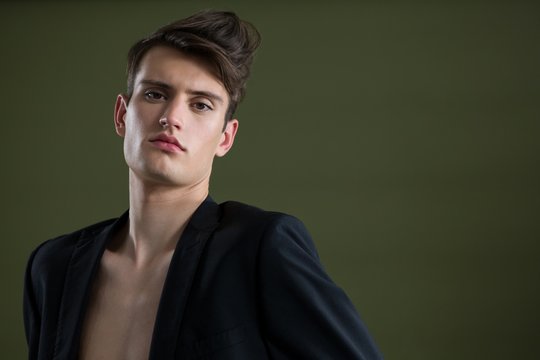 Androgynous man in blazer posing against green background