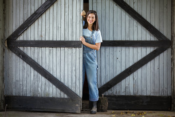 Young woman working on a farm is opening the door of a barn or shed © bokan