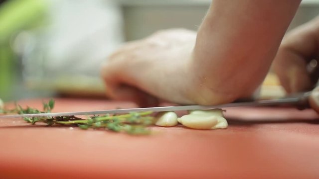 Clove of garlic is crushed on the kitchen table with a knife blade close-up, slow mo. Men's hands crushing garlic while cooking