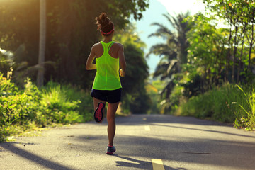 Young fitness woman running on morning tropical forest trail