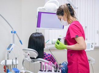 Dentist prepares to make tooth x-ray image for woman patient in dental clinic. Mobile portable x-ray device.