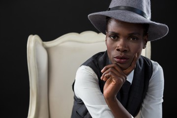 Androgynous man sitting on a chair with hand on chin