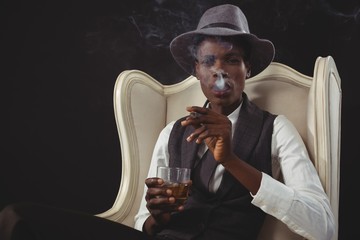 Androgynous man smoking cigar while while sitting on a chair 