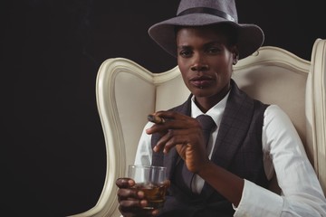 Androgynous man holding cigar while while sitting on a chair 