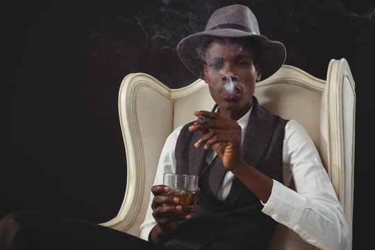 Androgynous man smoking cigar while while sitting on a chair