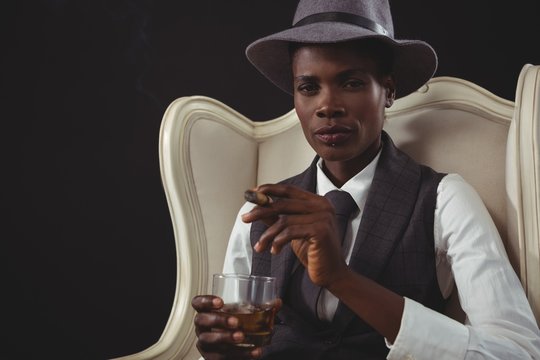 Androgynous man holding cigar while while sitting on a chair