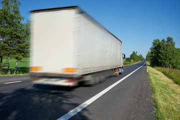 Motion blurred white truck driving on the road lined avenue of trees in a rural landscape on a bright sunny day