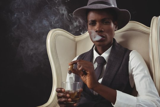 Androgynous man smoking cigar while while sitting on a chair