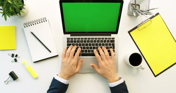 Business man working on laptop with green screen on office desk background. Man hands typing on laptop keyboard. Top view. Chroma key