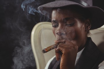 Androgynous person smoking cigar while sitting on a chair