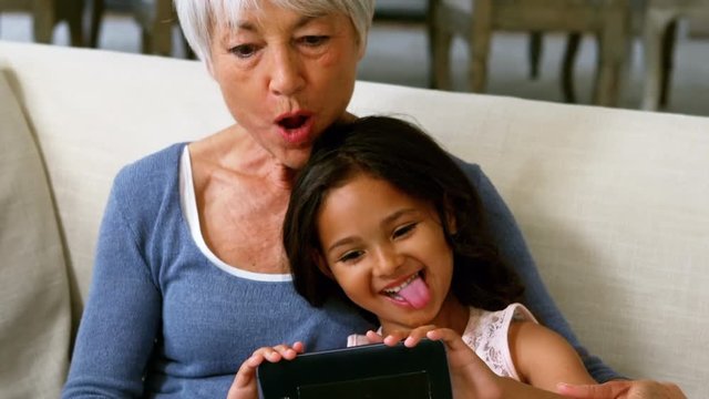 Granddaughter and grandmother taking selfie on mobile phone in living room