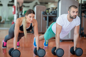 Fototapeta na wymiar Gym man and woman push-up strength pushup with dumbbell in a workout