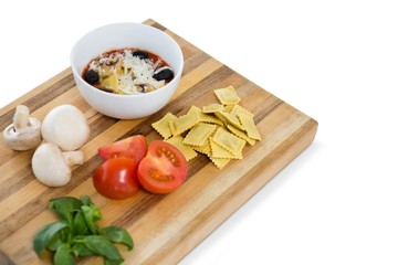 Cooked food in bowl by ravioli and vegetables on cutting board
