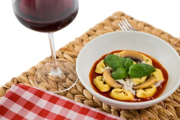 Close of cooked tortelloni in bowl on napkin by wineglass 